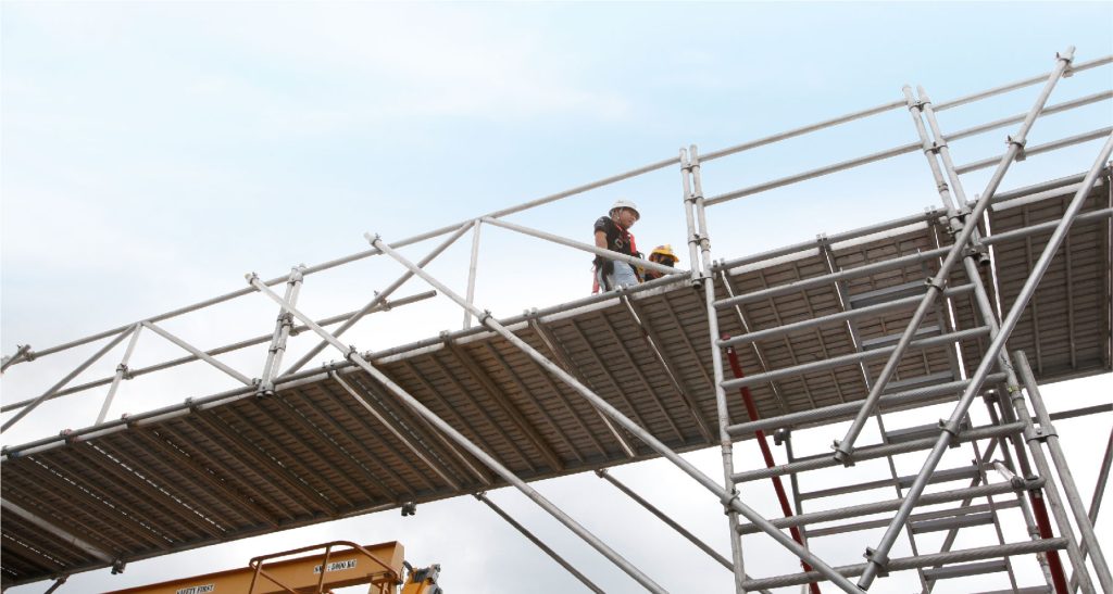 Construction workers on scaffolding installing aluminum curtain wall system for modern facade cladding.